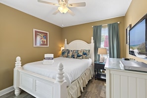A hotel room with a bed, a desk, a ceiling fan, a window with curtains, and a painting on the wall. - Panorama - Gulf Views! Heated Private and Community Pool! Free Beach Service! (Miramar Beach)