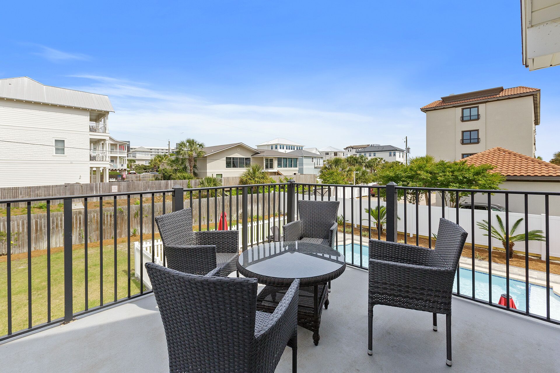 A balcony with wicker furniture and a view of a swimming pool and neighboring houses.