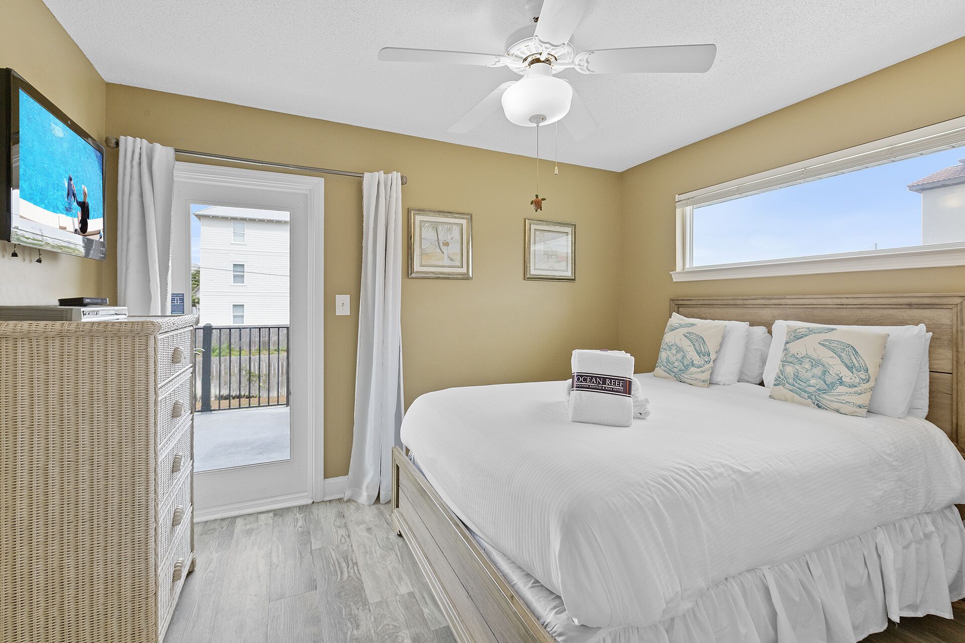 A bedroom with a bed, a ceiling fan, a window, and a door leading to a balcony.