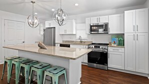 A modern kitchen with white cabinets, stainless steel appliances, a central island with bar stools, and pendant lighting.