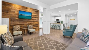 A modern living room with a wooden accent wall, a flat-screen TV, and a kitchen area with bar stools.