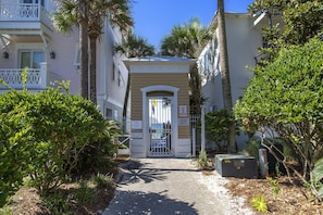 A narrow pathway leading to a gated entrance of a building with a covered porch and a mailbox.