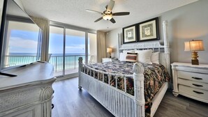 Una camera da letto con un letto, una ventola a soffitto, un comodino, una lampada, una cassettiera e un'ampia finestra vista oceano.