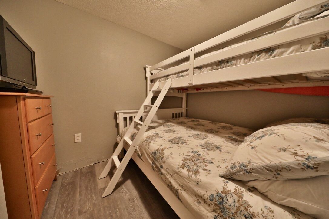 A bunk bed with a ladder, a wooden dresser, and a television on top.