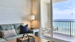 Una stanza con un divano verde, un tavolino in legno, una lampada e vista sull'oceano da un balcone.