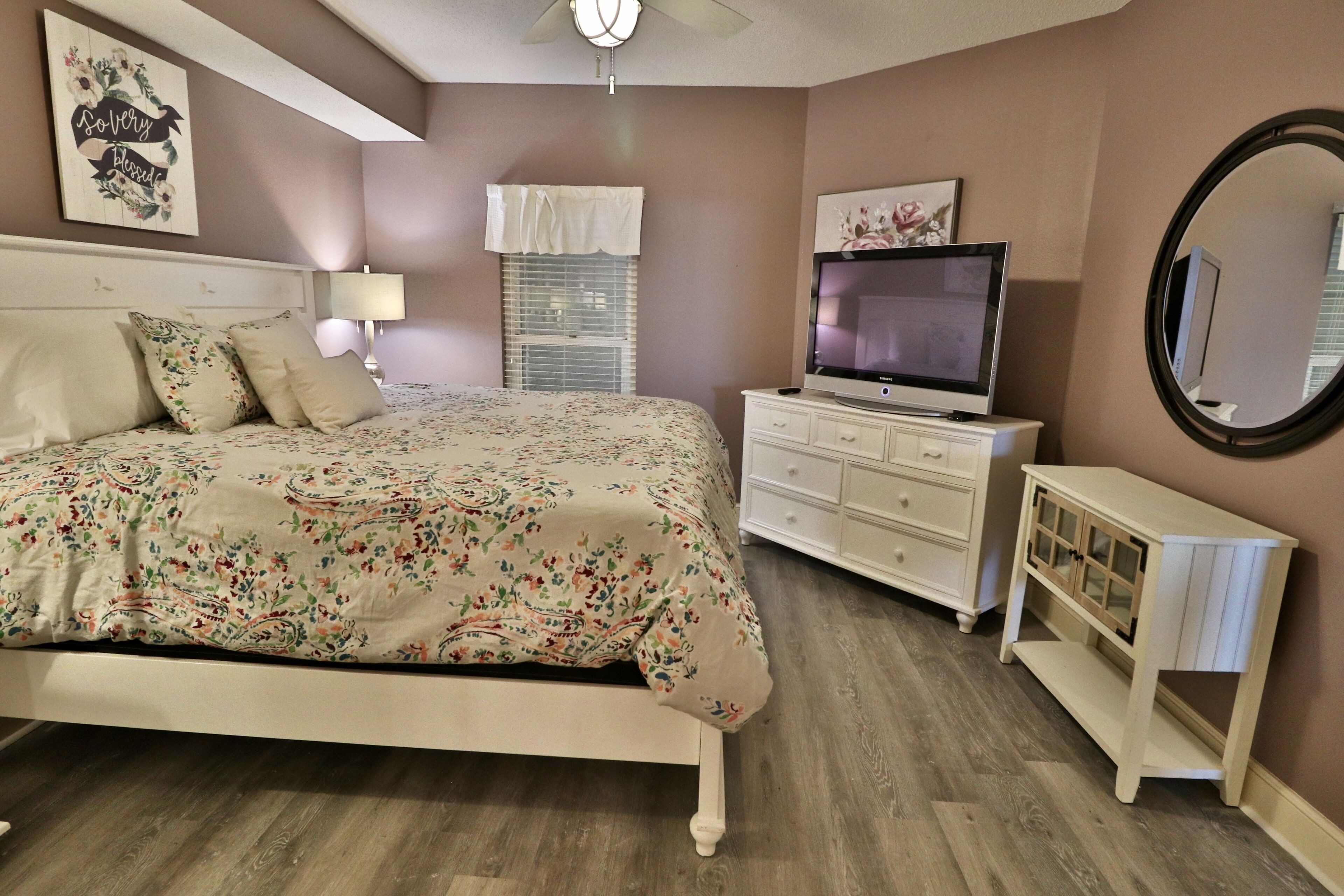 A bedroom with a bed, dresser, TV, and a mirror.