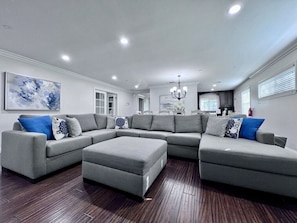 A modern living room with a sectional sofa, ottoman, and a chandelier.