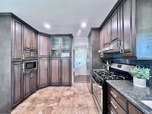 A kitchen with dark wood cabinets, a stainless steel range hood, a microwave, and a granite countertop.