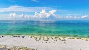 Uma praia com vista clara do oceano e uma área arenosa com guarda-sóis e cadeiras de praia dispostas em padrão.