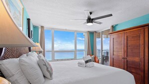 Quarto de hotel com uma cama grande, ventilador de teto e vista para o mar.