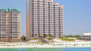 Hotel alto com várias varandas, próximo a uma praia com guarda-sóis e pessoas.