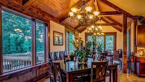A spacious dining area with a large wooden table and chairs, surrounded by large windows offering views of the outdoors. - On The Golf Course, Outdoor Kitchen, Hot Tub and So Much More! (Galena)
