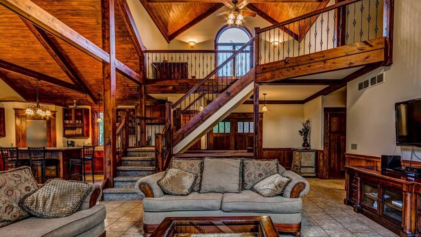 A spacious living room with a high ceiling, wooden beams, a staircase, and a large window. - On The Golf Course, Outdoor Kitchen, Hot Tub and So Much More! (Galena)