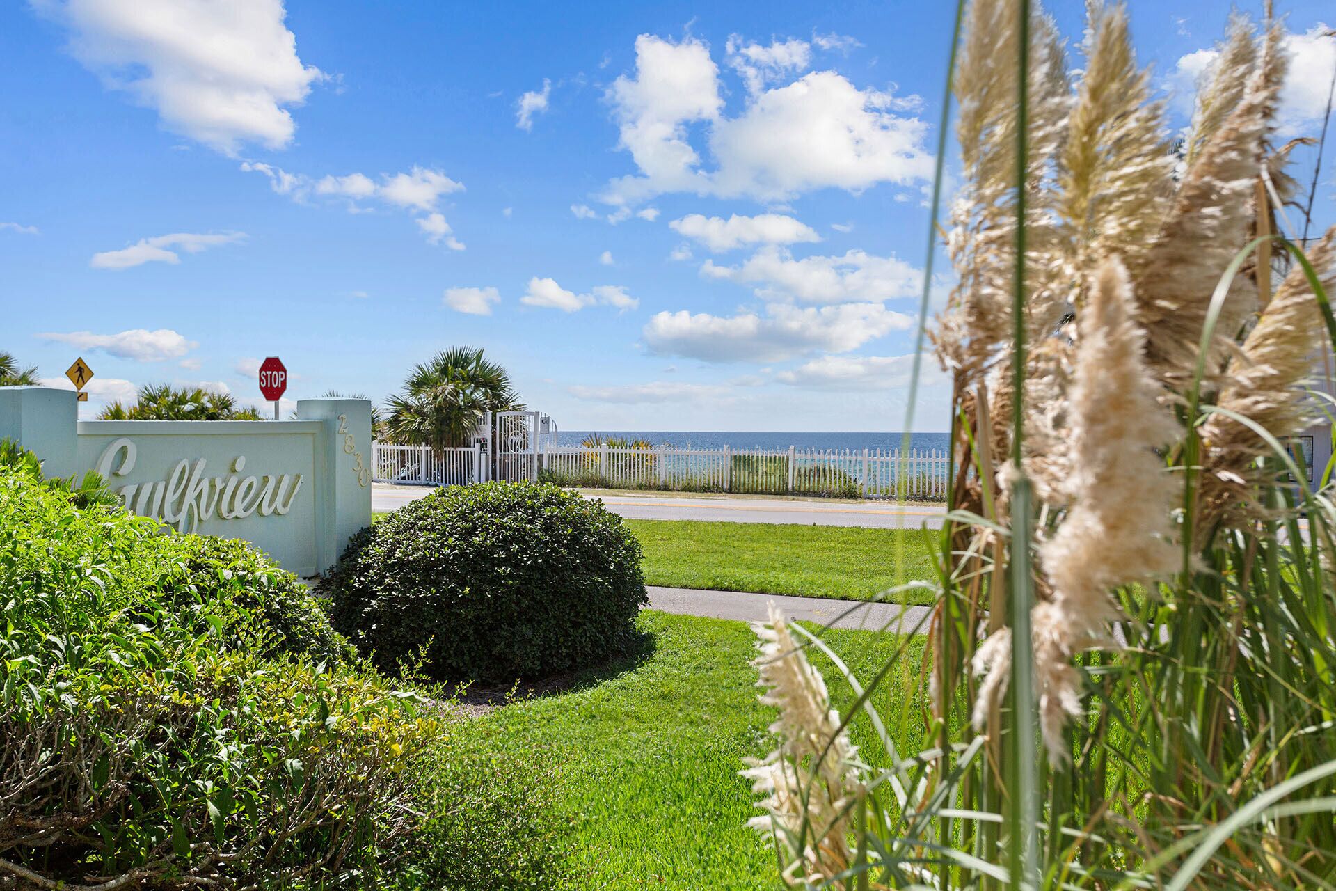 A sign with "Gulfview" written on it, a stop sign, a white fence, and a view of the ocean.