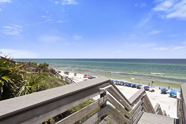 A wooden staircase leading to a beach with umbrellas and people.