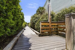 A wooden boardwalk leading to a gated entrance, surrounded by dense greenery.