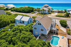 A residential area with a house featuring a pool, surrounded by lush greenery and a view of the ocean.