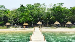 A wooden pier leading to a beach with thatched-roof huts and palm trees. - Hotel Casa Flores De Tikal (Flores)