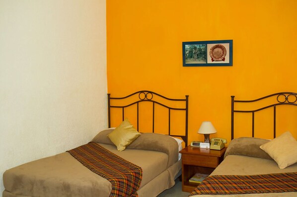 A room with two beds, each with a headboard and a bedside table. There is a framed picture on the wall above the beds. - Hotel Casa Flores De Tikal (Flores)