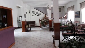 A spacious living area with a staircase, a purple reception desk, and a seating area with chairs. - Hotel Casa Flores De Tikal (Flores)