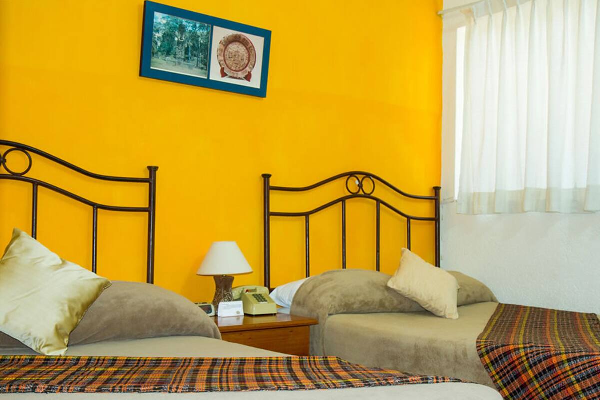 Ein Hotelzimmer mit zwei Betten, einem Nachttisch mit Lampe und Telefon sowie einem gerahmten Bild an der Wand.