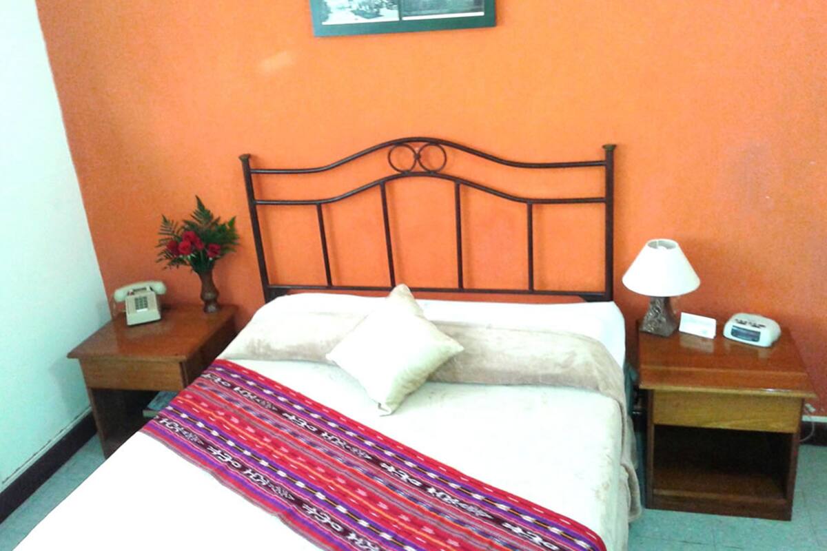Ein Zimmer mit einem Bett, einem Nachttisch mit Lampe, einem Telefon und einem gerahmten Bild an der Wand.