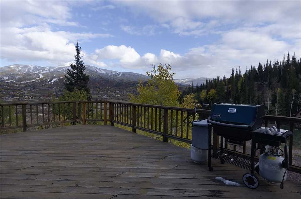 A wooden deck with a barbecue grill and trash bins, overlooking a mountainous landscape.