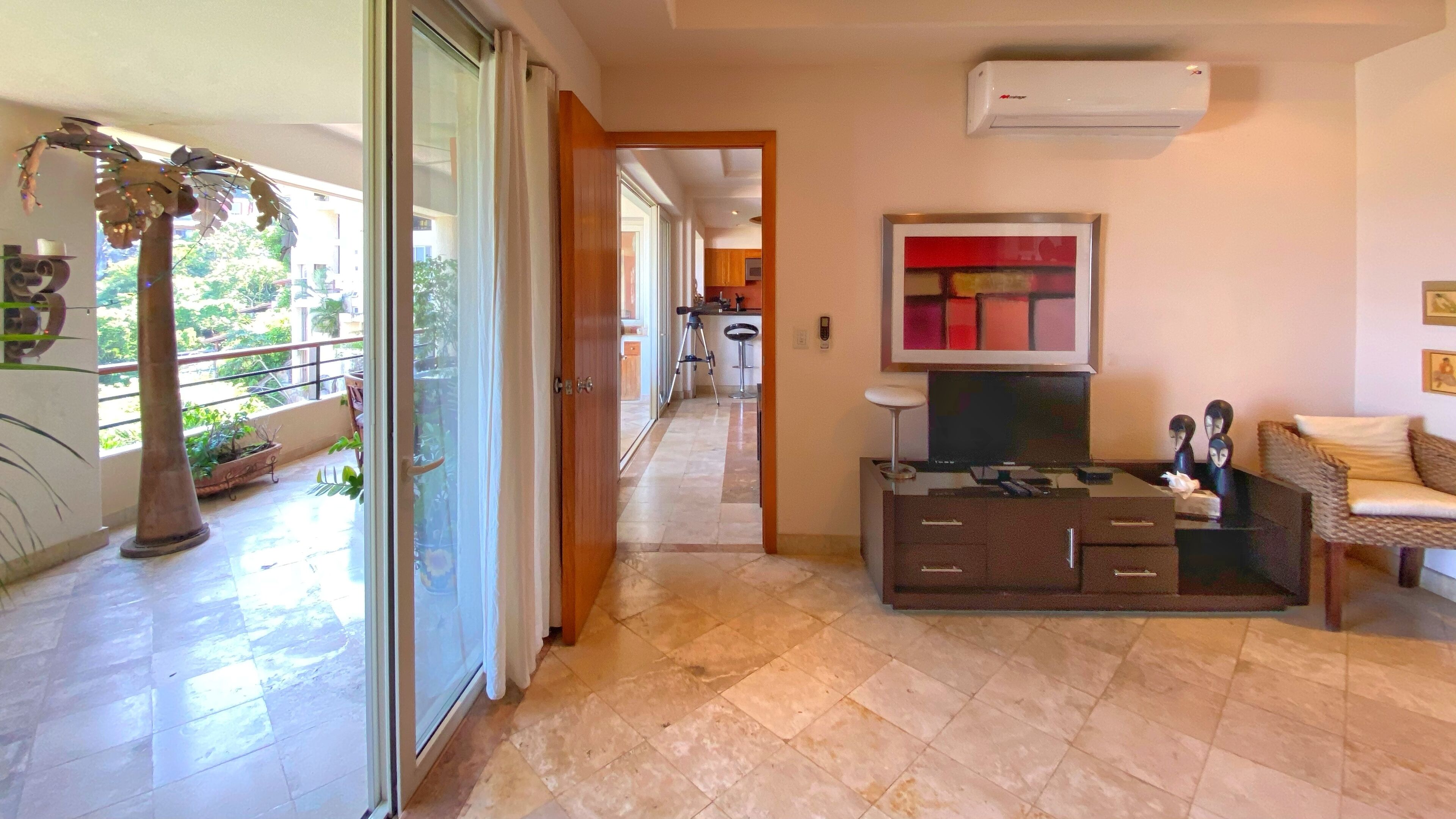 A living room with a glass door leading to a balcony, a TV, and a cabinet with drawers.