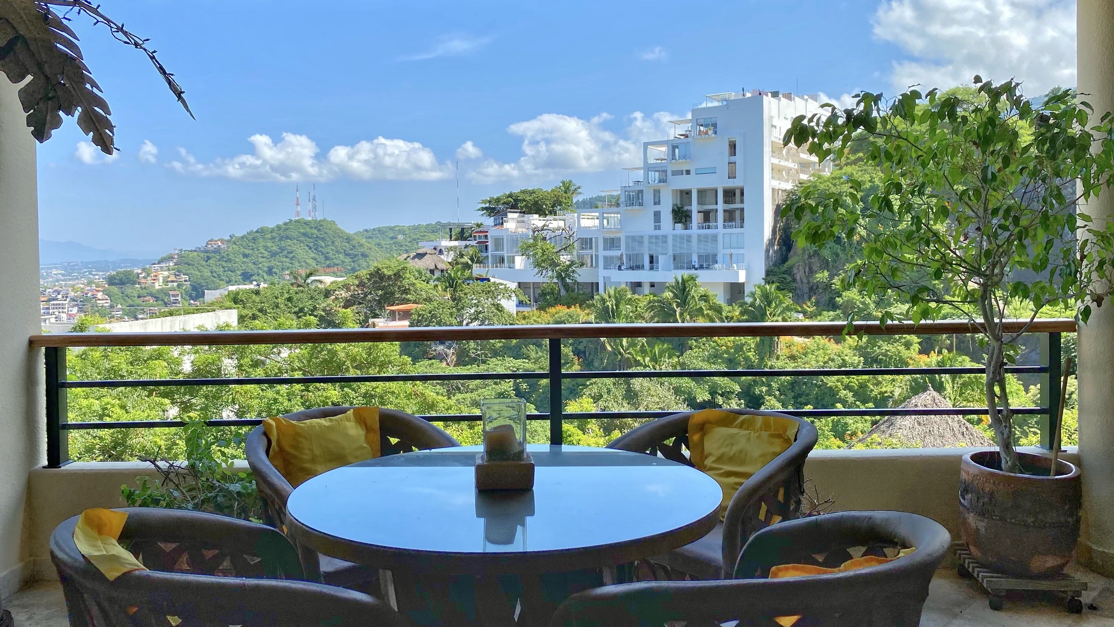 Un balcon avec une table ronde et des chaises, d’où l’on peut admirer un paysage urbain composé d’immeubles et d’espaces verts.