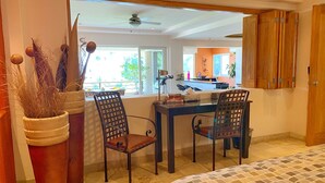 Un coin repas avec une table et des chaises, une plante en pot, et une vue sur la cuisine et le balcon.