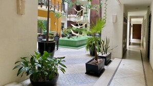Un couloir agrémenté de plantes en pot, un espace de détente verdoyant et une vue sur un immeuble à plusieurs étages doté de balcons.