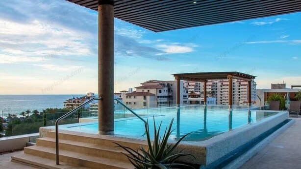 Une piscine à débordement située sur le toit, offrant une vue sur l’océan et un ensemble d’immeubles en arrière-plan.