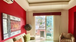 Un salon moderne avec un mur d’accent rouge, une grande peinture abstraite, un canapé avec des coussins, un fauteuil à motifs et une table basse en verre.