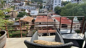 Un balcon agrémenté de meubles en osier, une vue sur une colline parsemée de bâtiments et un ciel dégagé.