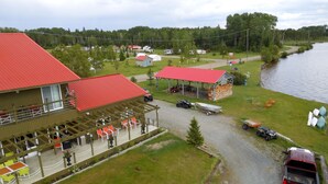 Un bâtiment situé au bord du lac, avec un toit rouge, des tables à l’extérieur et un quai.