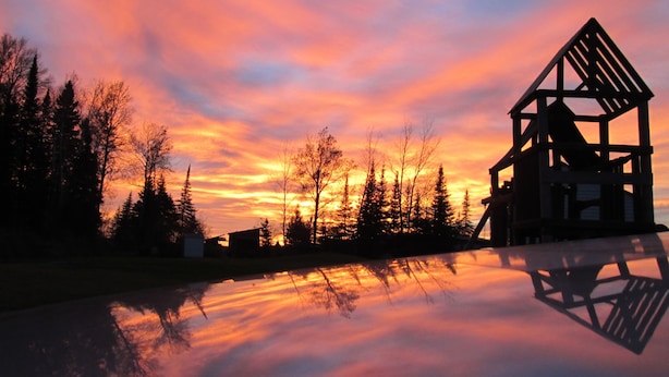 Une cabane en bois dont le toit triangulaire se découpe sur le ciel au coucher du soleil.