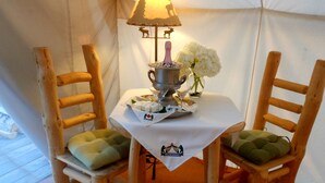 Une tente avec une table dressée pour deux personnes, comprenant une casserole en métal, un verre et un vase avec des fleurs blanches.