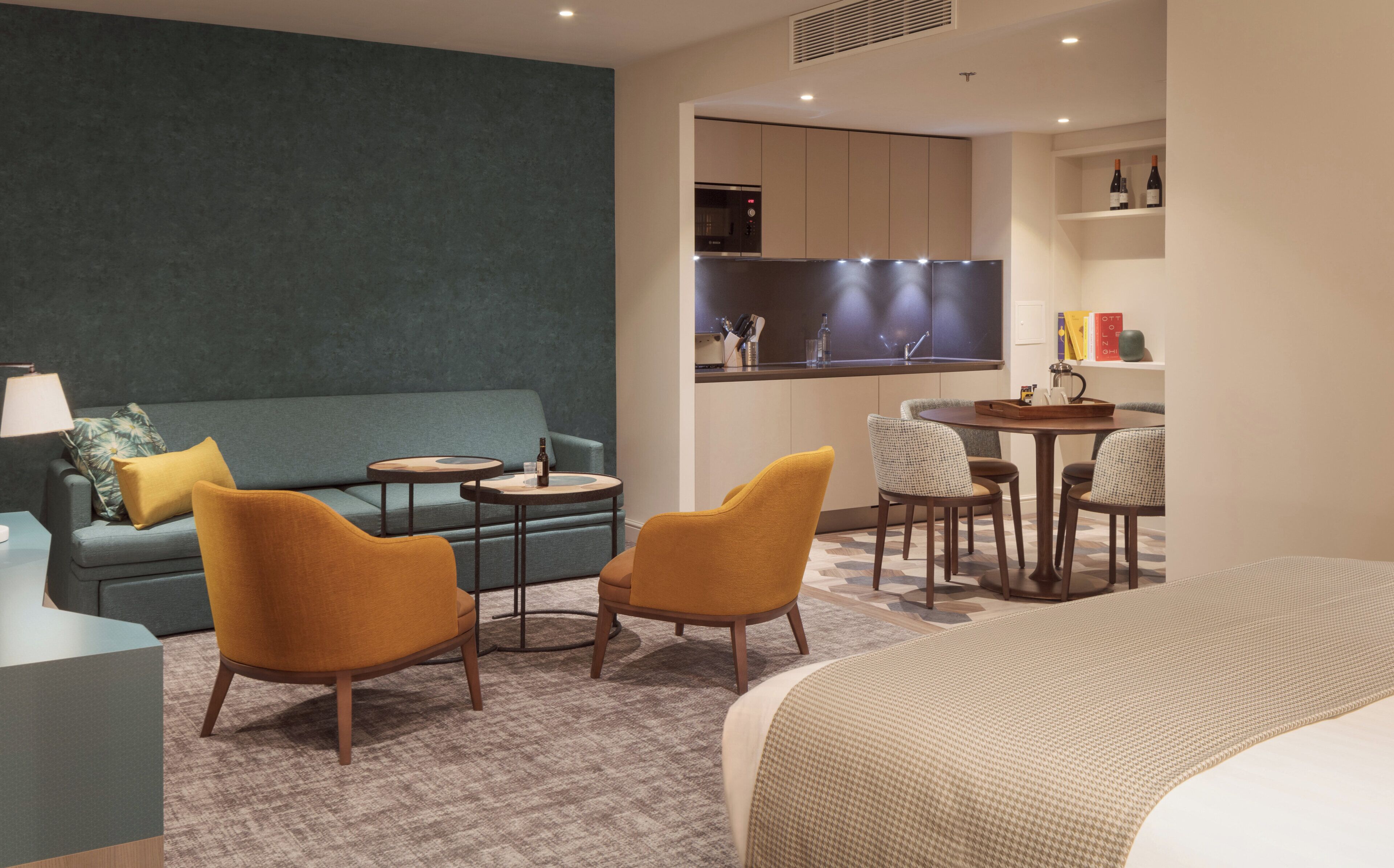 Ein Hotelzimmer mit einer Couch, zwei Sesseln, einem kleinen Tisch, einem Bett, einer Küchenzeile und einem Essbereich.