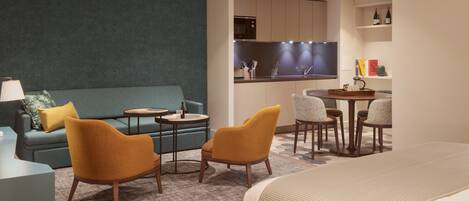 A modern hotel room with a sofa, two armchairs, a small round table, and a bed.
