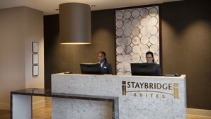 A reception desk at Staybridge Suites with a marble design, framed certificates on the wall, and a modern pendant light. - Staybridge Suites London Heathrow - Bath Road by IHG (West Drayton)