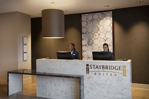 A reception desk at Staybridge Suites with a marble design, framed certificates on the wall, and a modern pendant light. - Staybridge Suites London Heathrow - Bath Road by IHG (West Drayton)