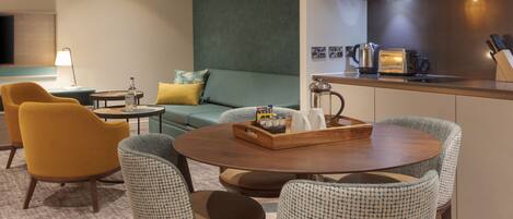 Una sala moderna con un sofá, dos sillones, una mesa de centro y una zona de cocina con microondas y tostadora.
