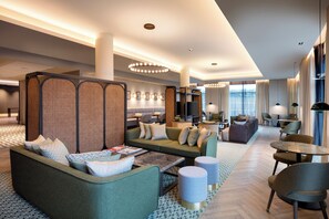 A modern hotel lobby with seating areas, a television, and a large window with curtains. - Staybridge Suites London Heathrow - Bath Road by IHG (West Drayton)