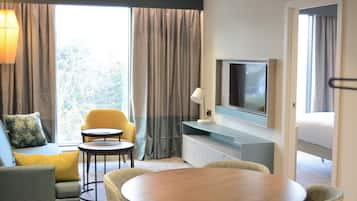 Ett hotellrum med en soffa, två fåtöljer, ett runt bord, en tv och ett fönster med gardiner.