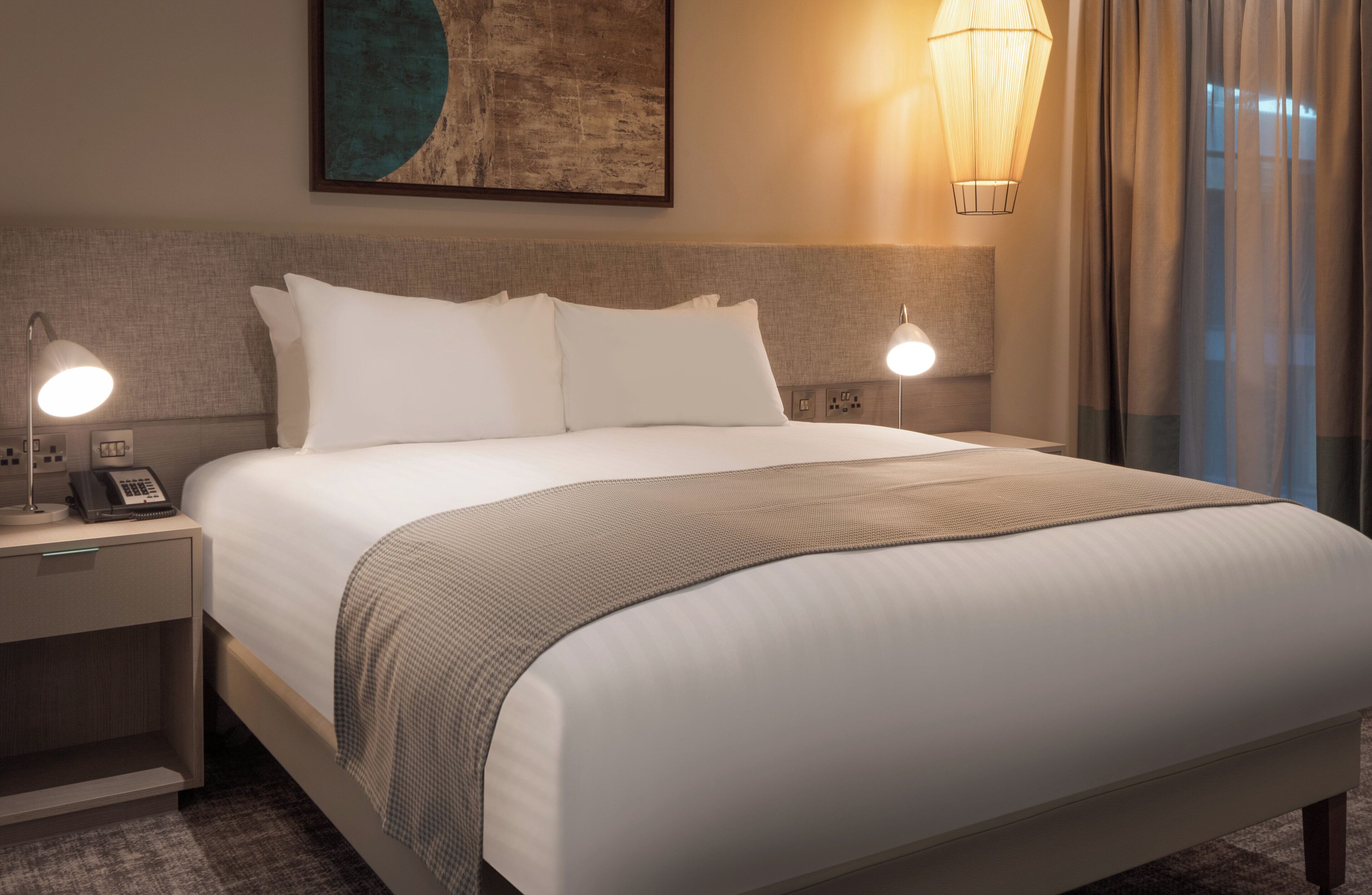 A hotel room with a large bed, bedside lamps, a telephone, and a painting on the wall.