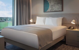 Una habitación de hotel con una cama grande, dos lámparas de noche, un teléfono y un cuadro sobre la cama.