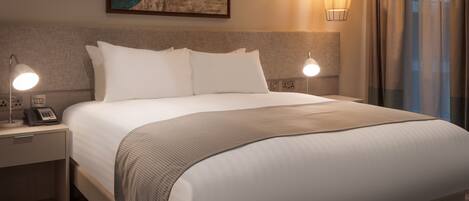Ein Hotelzimmer mit einem großen Bett, zwei Nachttischlampen, einem Telefon und einem Gemälde an der Wand.