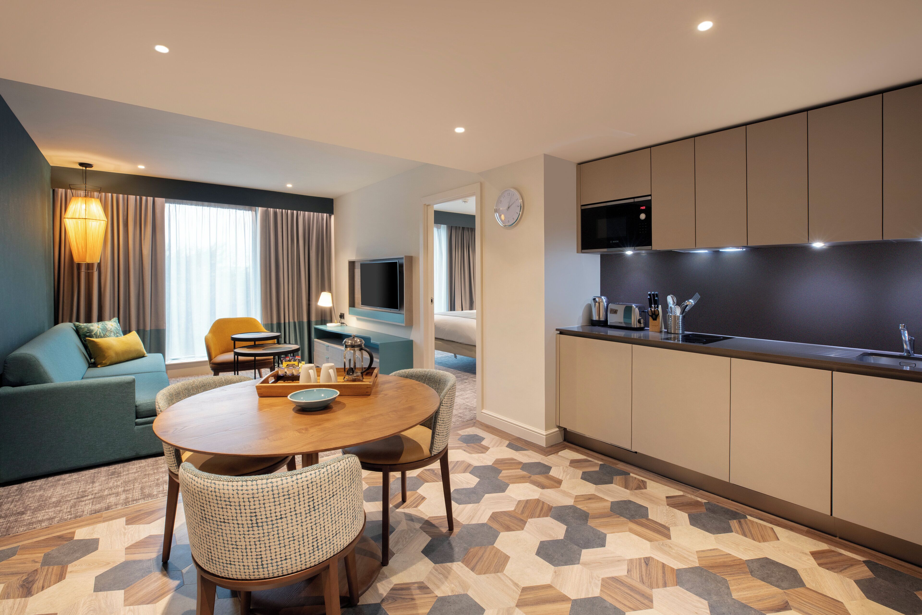 A modern hotel room with a dining area, kitchenette, and a living space.
