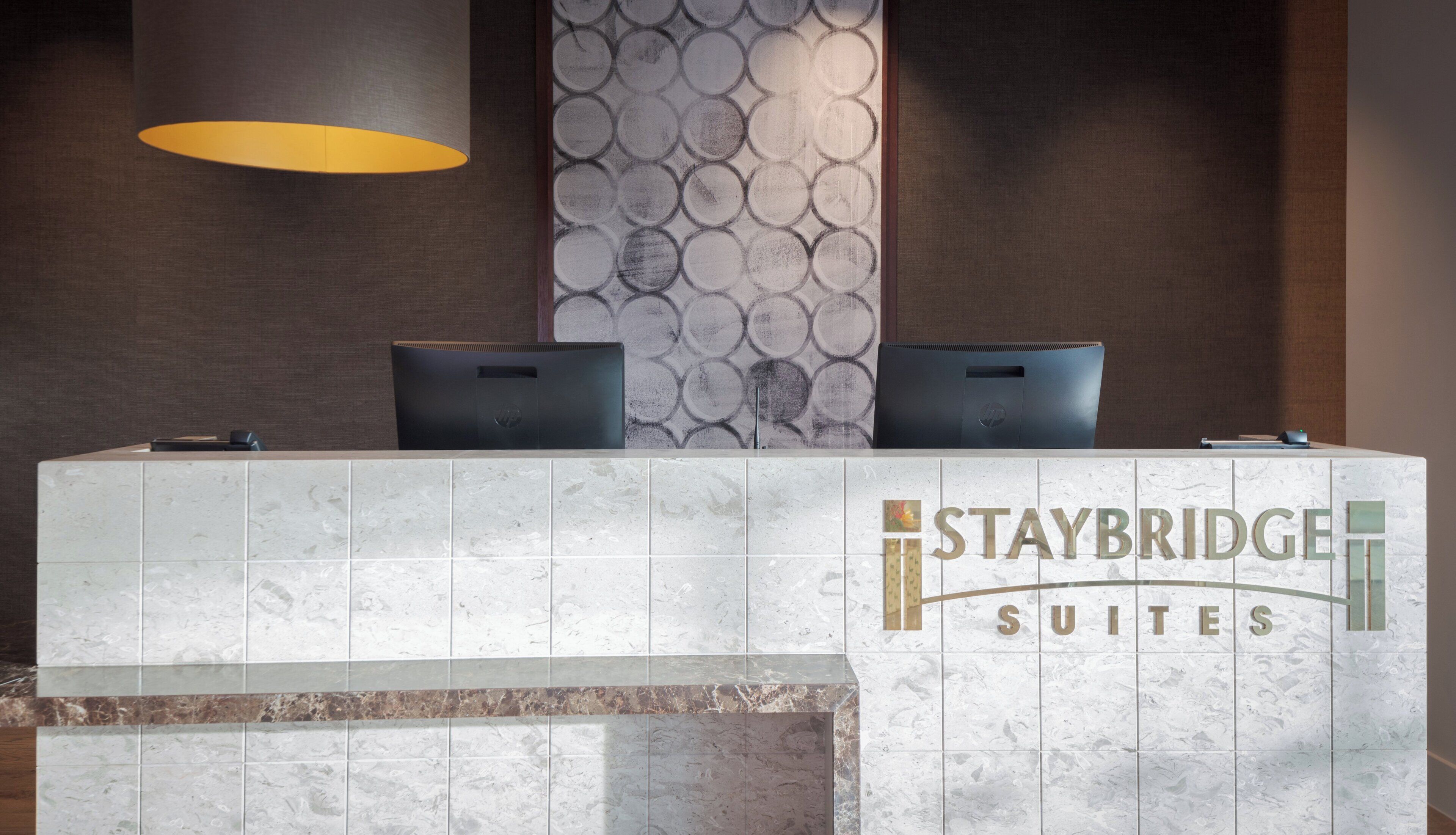 A reception desk with two laptops, a lamp, and a wall with a circular pattern.