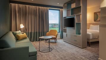 A hotel room with a sofa, armchair, TV, and a bed.